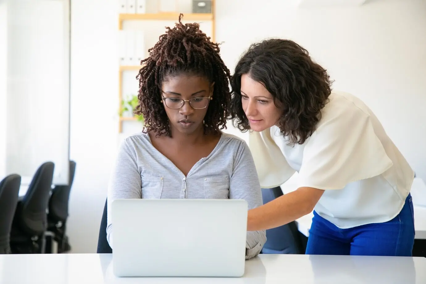Frontalansicht selbstbewusster Frauen, die sich unterhalten, während sie an einem Laptop arbeiten.
